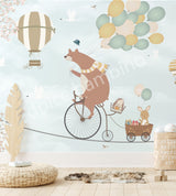 A wall mural featuring a cartoon bear riding a bicycle with a hot air balloon and various other playful animals, on a blue background.