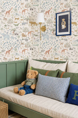 A styled children's bedroom corner featuring a green daybed with cream cushions, patterned pillows, a teddy bear, and a wall covered in safari-themed animal wallpaper.