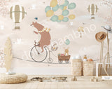 A wall mural featuring a cartoon bear riding a bicycle with a hot air balloon and various other playful animals, on a beige background.