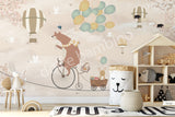 A wall mural featuring a cartoon bear riding a bicycle with a hot air balloon and various other playful animals, on a beige background.