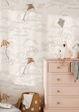 A styled nursery room corner featuring wallpaper with a whimsical cloud and kite pattern, a light pink wooden dresser, and decorative flamingo figurines.