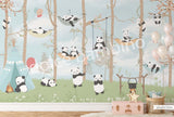 A wall mural featuring cartoon pandas in a forest setting, with trees and a blue sky, applied in a room with a crib and wooden furniture.