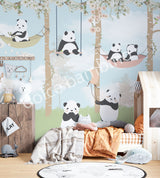 A wall mural featuring cartoon pandas in a forest setting, with trees and a blue sky, applied in a room with a bed and wooden furniture.