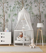 A nursery room with a crib, white furniture, and a wall mural featuring green birch trees.
