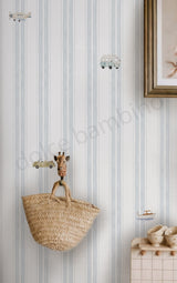 A styled interior scene showing a woven straw tote bag hanging on striped wallpaper.