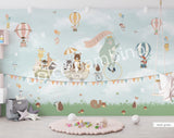 A whimsical wall mural featuring a bear on a bicycle with a wagon full of various cartoon animals, set against a grey background with hot air balloons and a cloudy sky.