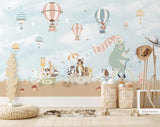 Large nursery wall mural in blue brown and beige tones featuring hot air balloons floating among birds and cherry blossom branches. A mint-green bear rides a vintage bicycle while woodland animals travel in a wagon below, creating a whimsical storybook scene for a baby's room