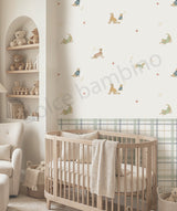 A styled nursery room featuring a wall with a repeating pattern of classic cartoon dog characters in blue and green, set against a warm cream background. A light wood crib with cream bedding is positioned in the foreground, alongside a beige armchair and a built-in wooden shelf with teddy bears.