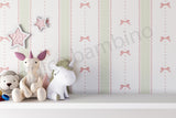 A styled nursery scene featuring a wall with vertical green and white gingham stripes, pink bow motifs, and scalloped borders, with plush toys including a unicorn and a bear sitting on a white shelf in front.