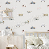 Childhood bedroom wallpaper featuring a playful pattern of vintage toy cars, trucks, bicycles, boats, and airplanes in muted pastel colors on a warm off-white background. The wallpaper is shown in a styled room setting with a light wood bed, white pillows, and a matching wooden storage cabinet.