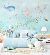 A room with 'Under the Sea' themed wallpaper featuring illustrations of sea creatures such as an octopus, whale, sea horses, and starfish in pastel colors. The room is styled with sea-themed bedding, a sofa, and decorative items.