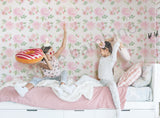 Two children playing on a bed with floral wallpaper in the background