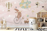 A wall mural featuring a cartoon bear riding a bicycle with a hot air balloon and various other playful animals, on a dusty rose background.