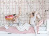 Two children playing on a bed with floral wallpaper in the background