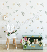 A wall adorned with a floral and leaf pattern wallpaper, featuring a white chair, a green trunk, and decorative flowers in the foreground.