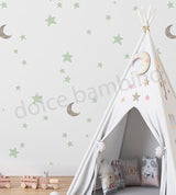 White children's teepee with decorative pillows and toys against a wall with star and moon wallpaper.