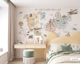 Children's room featuring a colorful world map wallpaper with illustrations of animals and vehicles. A wooden dresser and a canvas storage basket are visible in the room.
