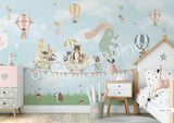 A whimsical wall mural featuring a bear on a bicycle with a wagon full of various cartoon animals, set against a grey background with hot air balloons and a cloudy sky.