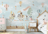 A whimsical wall mural featuring a bear on a bicycle with a wagon full of various cartoon animals, set against a pink background with hot air balloons and a cloudy sky.