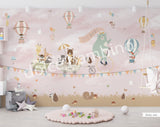 A whimsical wall mural featuring a bear on a bicycle with a wagon full of various cartoon animals, set against a pink background with hot air balloons and a cloudy sky.