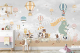 Large nursery wall mural in grey and beige tones featuring hot air balloons floating among birds and cherry blossom branches. A mint-green bear rides a vintage bicycle while woodland animals travel in a wagon below, creating a whimsical storybook scene for a baby's room