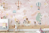 Large nursery wall mural in soft pink and beige tones featuring hot air balloons floating among birds and cherry blossom branches. A mint-green bear rides a vintage bicycle while woodland animals travel in a wagon below, creating a whimsical storybook scene for a baby's room