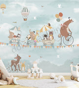 A children's wall mural featuring an illustration of a bear riding a bicycle with various animals such as a hedgehog, raccoon, elephant, panda, and fox in a wagon, against a sky filled with hot air balloons and birds.