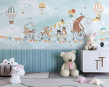 A children's wall mural featuring an illustration of a bear riding a bicycle with various animals such as a hedgehog, raccoon, elephant, panda, and fox in a wagon, against a sky filled with hot air balloons and birds.