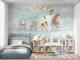 A children's wall mural featuring an illustration of a bear riding a bicycle with various animals such as a hedgehog, raccoon, elephant, panda, and fox in a wagon, against a sky filled with hot air balloons and birds.
