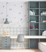 A styled children's room corner featuring a gray desk, gray chair, and a large dark gray bookshelf. The wall behind is decorated with a light wallpaper pattern of small dog illustrations and a blue-and-white checkered wainscoting panel.