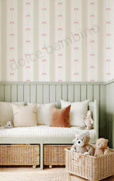 A styled children's room corner featuring light green and cream wallpaper with a repeating bow pattern, a pale green wooden bench with woven storage baskets underneath, striped and solid throw pillows, and two wicker baskets containing stuffed toys in the foreground.