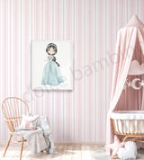 A framed wall art print featuring a cartoon girl in a light blue dress hanging on a pink and white striped wallpapered wall in a styled nursery. A wooden chair with a throw blanket, a pink canopy crib, and a star pillow are visible.