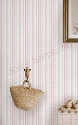 Pink and white striped wallpaper with small gold dots, styled with a woven straw basket hanging from a giraffe-shaped hook on a wooden wall.