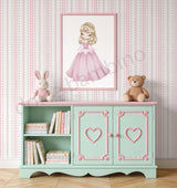 A styled children's room scene featuring a mint green and pink wooden side cabinet with heart-shaped door details, topped with a framed illustration of a girl in a pink dress. The cabinet is decorated with books, and a plush bunny and teddy bear sit on top against a pink and white striped wallpaper background.