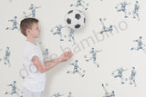 a boy standing against a wall with soccer-themed wallpaper.