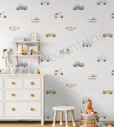 A children's nursery wall decorated with light blue and beige vehicle decals, including cars, trucks, buses, and bicycles, shown above a white dresser with toys and a small wooden stool.