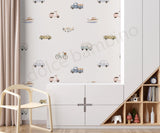A children's room interior featuring a wall covered in a repeating pattern of vintage-style vehicles such as cars, trucks, bicycles, boats, and airplanes on a light background. A cream chair, white storage cabinet, beige curtains, and a wooden shelf with toys are visible in the room.