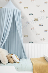 A styled children's bedroom corner featuring a light blue canopy bed with a pale blue quilt and beige pillows, set against a wall with white wainscoting and colorful vintage-style vehicle wallpaper decals.