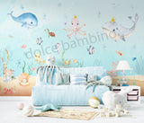 A room with 'Under the Sea' themed wallpaper featuring illustrations of sea creatures such as an octopus, whale, sea horses, and starfish in pastel colors. The room is styled with sea-themed bedding, a sofa, and decorative items.