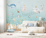 A room with 'Under the Sea' themed wallpaper featuring illustrations of sea creatures such as an octopus, whale, sea horses, and starfish in pastel colors. The room is styled with sea-themed bedding, a sofa, and decorative items.